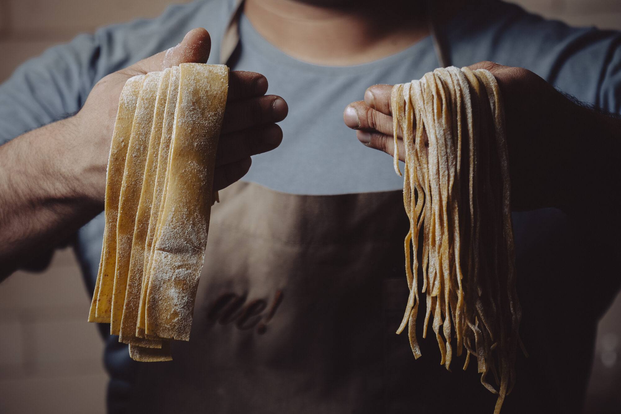 Cozinheiro segurando pappardelle e linguine frescos, feitos na casa